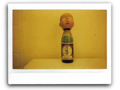 an instant picture of a babydoll head with clay over the eyes mounted on an empty sake bottle