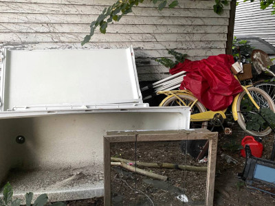 a backyard cluttered with a medicine-cabinet mirror, a tub, and a yellow bike draped in red cloth