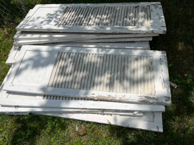 a pile of big white shutters lying in the grass in the shade of a tree