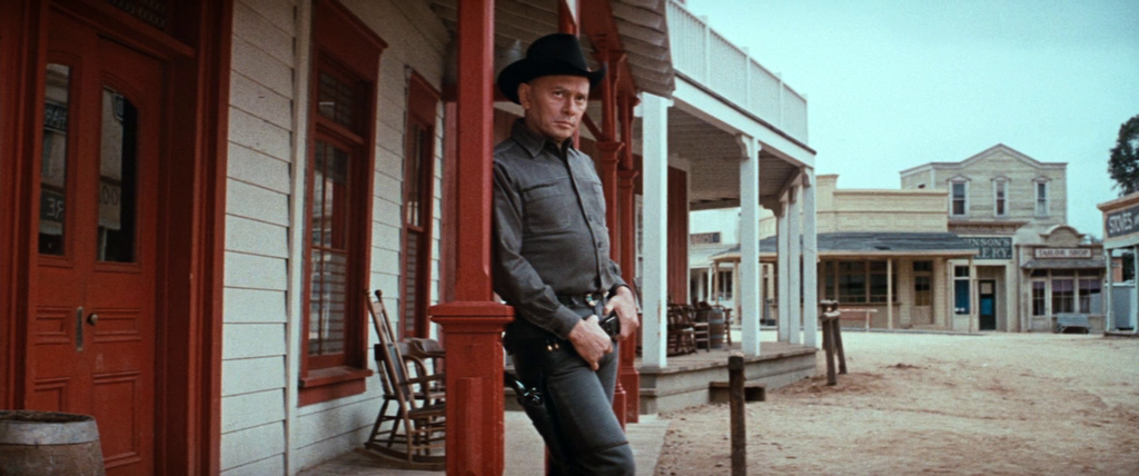 a screenshot from the film 'westworld' (1973) showing a gay cowboy robot leaning up against a column on a porch