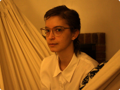 madi sitting in a white hammock in our living room. she has short hair and is wearing a white button-down with small gold hoop earrings in her ears. she is looking at the camera, and is the most beautiful human i've ever seen